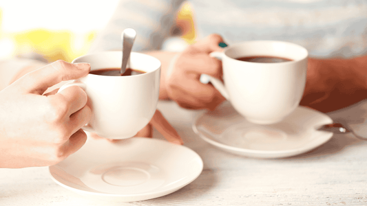 Two people holding white coffee cups with saucers, enjoying a warm beverage together.